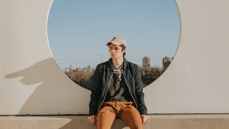 Teenager wearing a cap sitting down in the sun with a scenic background