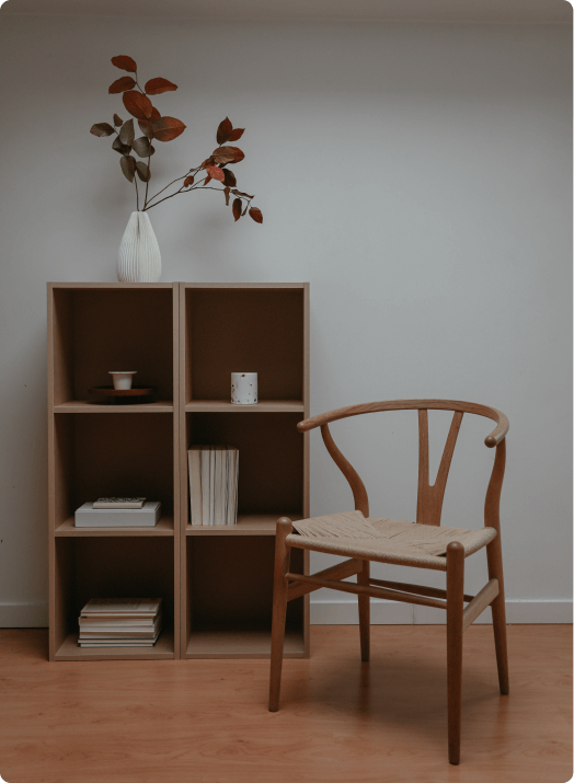 Photograph of a chair, bookshelf and jar of flowers