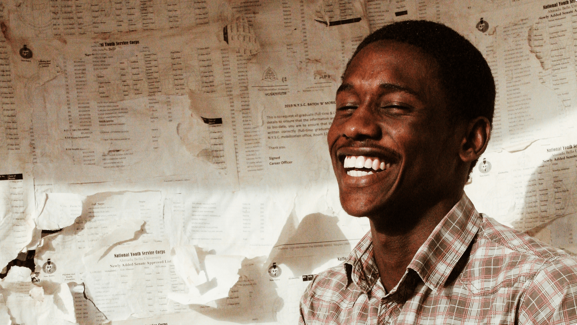 Photograph of a man smiling with joy, with papers on the wall