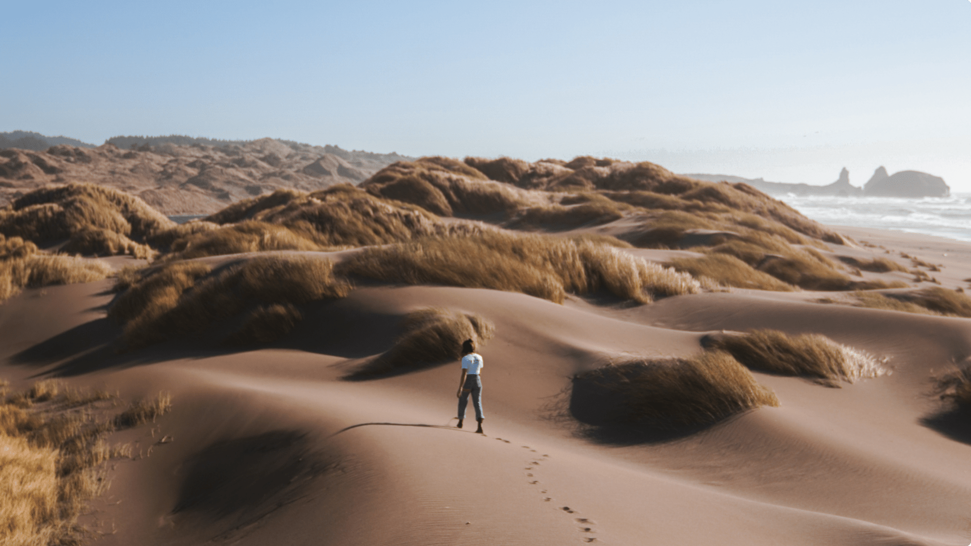 Woman walking through sand dunes, leaving footprints in the sand
